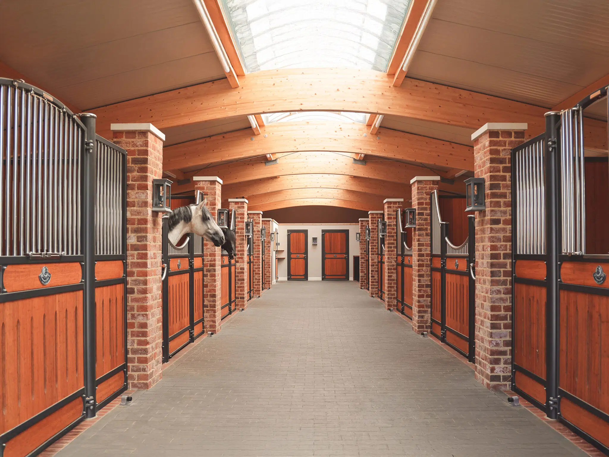 Sunlit Röwer & Rüb stable aisle with timber beams, brick pillars and horses